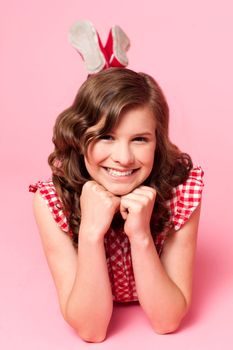 Happy young girl lying on floor. Hands on chin. All on pink background
