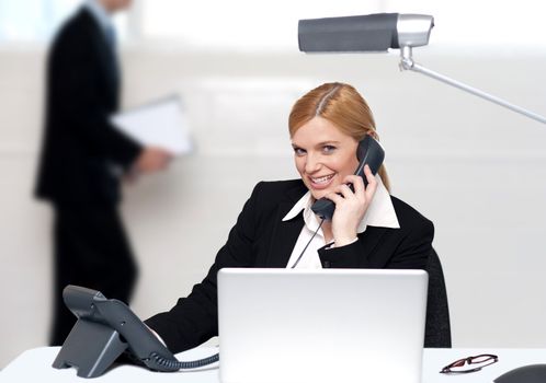 Attractive secretary attending phone call while man walk by in background