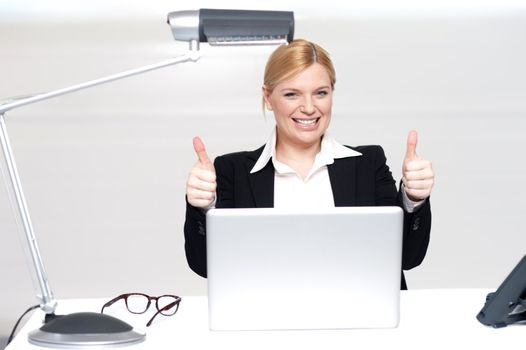 Cheerful businesswoman in office with laptop gesturing double thumbs up