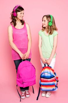 Beautiful teenagers standing with bag in hand and listening to music through headphones