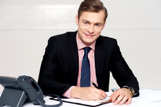 Handsome young businessman making notes, writing on notepad
