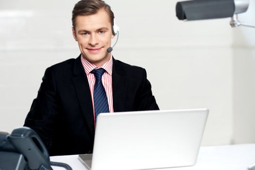 Smiling call centre executive posing with headsets. working on laptop