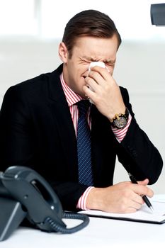 Young man having severe cold. Sneezing and cleaning nose with tissue paper