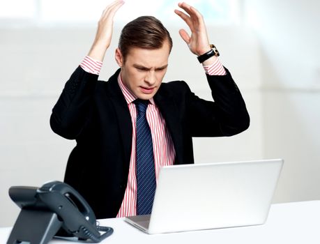 Disappointed businessman looking at laptop with hands above his head