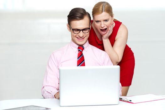 Shocked woman looking into laptop. Man working and smiling