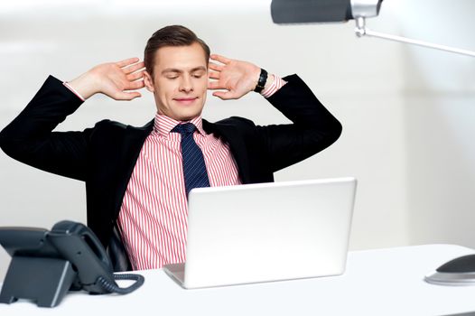 Young businessman posing in a relaxed manner with hands behind head looking at his laptop