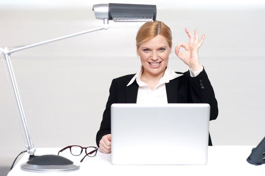 Corporate lady showing excellent gesture. Sitting at work desk