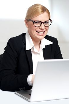Smiling young female executive at work desk operating on laptop
