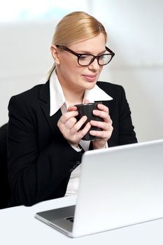 Female executive looking at laptop and holding coffee mug in hands