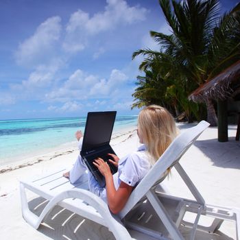 business woman with laptop lying on a chaise lounge in the tropical ocean coast