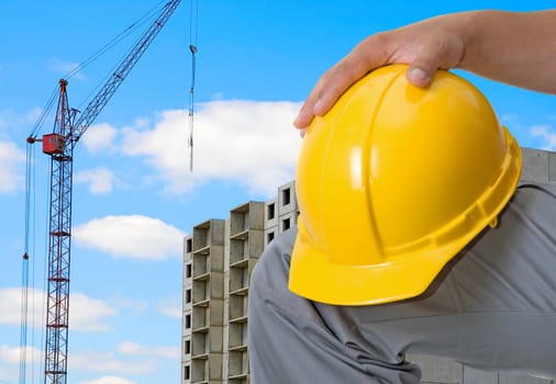 Closeup  of yellow helmet at builder hands on building background
