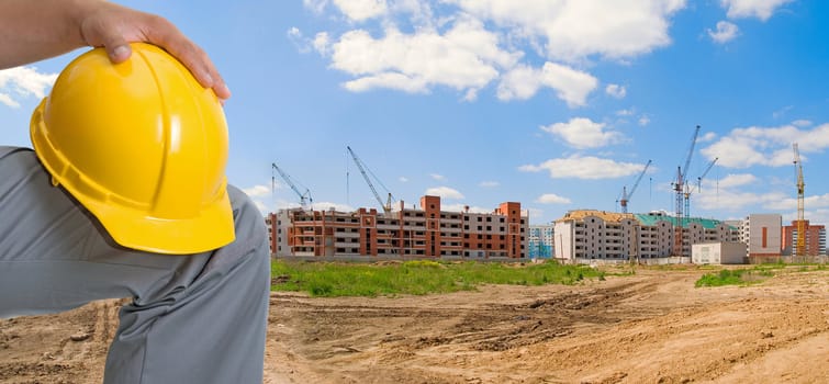 Closeup of yellow helmet at builder hands on building background