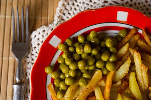 French fried potatoes with green peas on a plate served with fork and knife