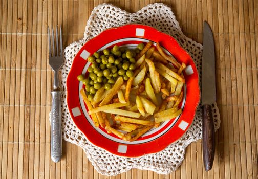 French fried potatoes with green peas on a plate served with fork and knife