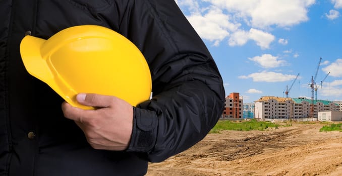 Closeup  of yellow helmet at builder hands on building background