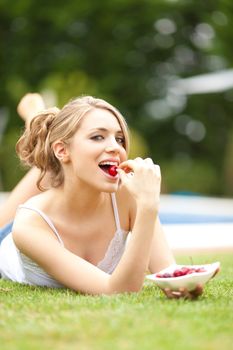 young beautiful blonde girl eating cherries on the grass