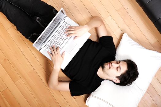 A young hispanic man surfing with a Laptop on the floor.
