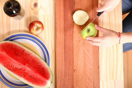 A young adult woman cutting fruits in the kitchen.