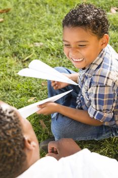 Happy Mixed Race Father and Son Playing with Paper Airplanes in the Park.
