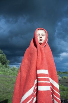 The girl wrapped in a red blanket on the background of a stormy sky