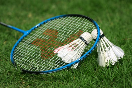 two shuttlecocks and badminton racket lying on the grass