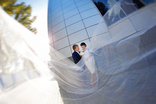 bride and groom by the wall with long flying veil