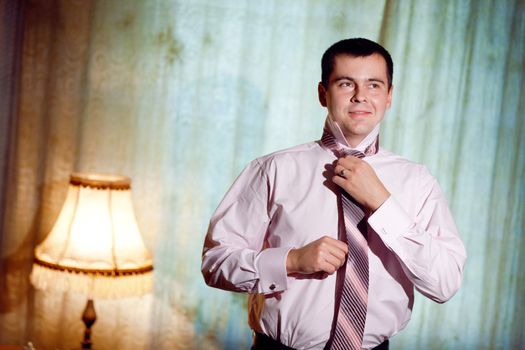 portrait of a young man putting on a necktie