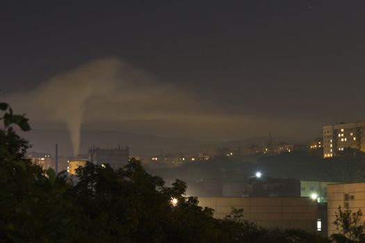 Smoke from a pipe in the city at night