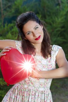 Attractive happy smiling brunette woman holding one red valentine heart, woman on park, concept of valentine's day