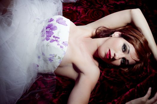 Beautiful redhead with long hair lying on a bed of roses