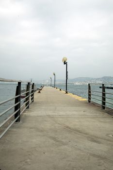 Cement pier with lamps on cloudy day with Cannes France in the background.