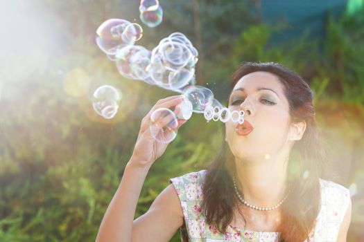 romantic young woman inflating colorful soap bubbles in spring park