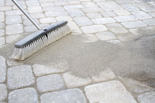 Broom Sweeping Locking Sand Into Backyard Patio Pavers