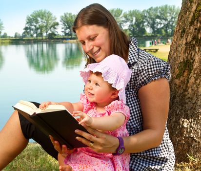 beautiful little girl reading book with her mother