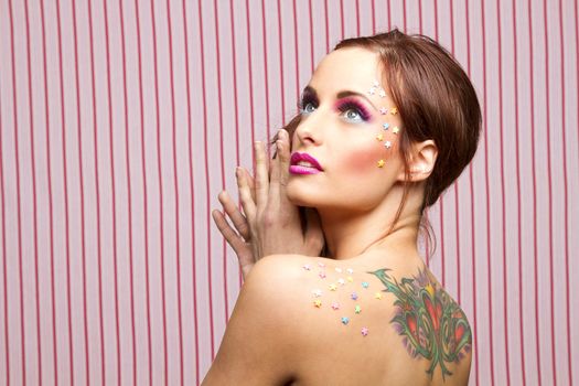 Young woman with colorful makeup and star candy glued to her face and back, looking up