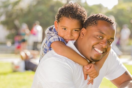 Happy African American Father and Mixed Race Son Playing Piggyback in the Park.