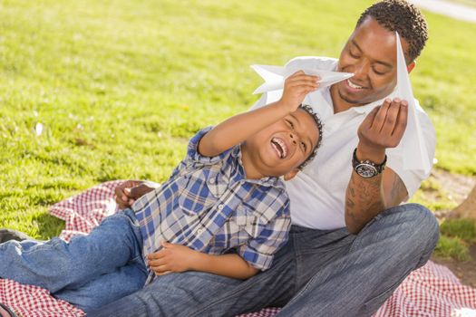Happy African American Father and Mixed Race Son Playing with Paper Airplanes in the Park.
