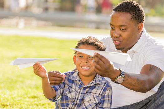 Happy African American Father and Mixed Race Son Playing with Paper Airplanes in the Park.
