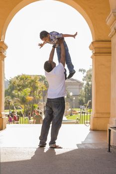 Happy African American Father Lifts Mixed Race Son Over His Head in the Park.