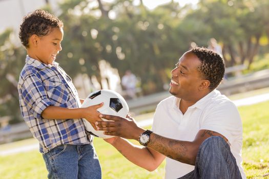 African American Father Hands New Soccer Ball to Mixed Race Son at the Park.
