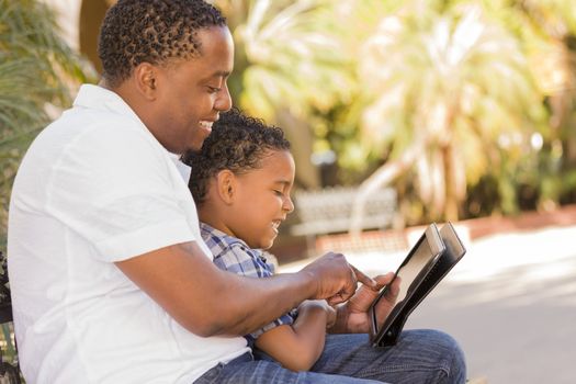 Happy African American Father and Mixed Race Son Having Fun Using Touch Pad Computer Tablet Outside.