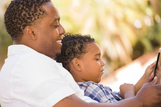 Happy African American Father and Mixed Race Son Having Fun Using Touch Pad Computer Tablet Outside.