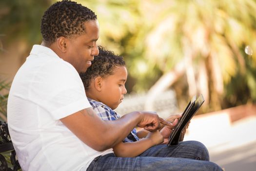 Happy African American Father and Mixed Race Son Having Fun Using Touch Pad Computer Tablet Outside.