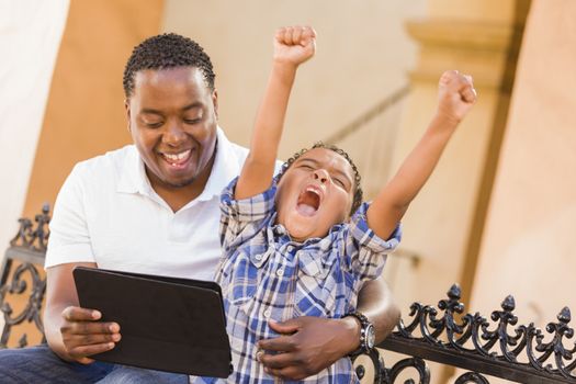 Happy African American Father and Mixed Race Son Having Fun Using Touch Pad Computer Tablet Outside.