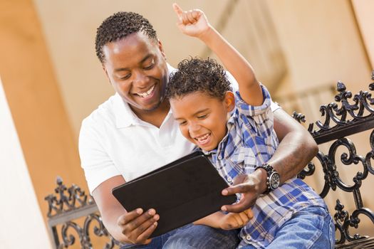 Happy African American Father and Mixed Race Son Having Fun Using Touch Pad Computer Tablet Outside.