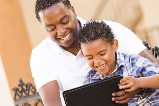 Happy African American Father and Mixed Race Son Having Fun Using Touch Pad Computer Tablet Outside.