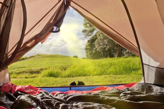 Campsite nature view of lush green countryside from inside a tent with sleeping bags laid out on the floor