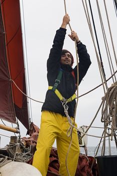 Young sailor on a ship's deck hoisting a sail