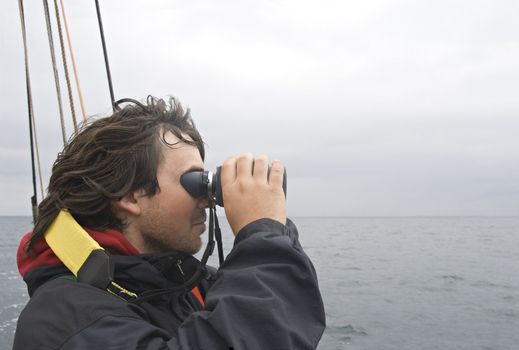 Young sailor looking in binoculars from a board of a ship