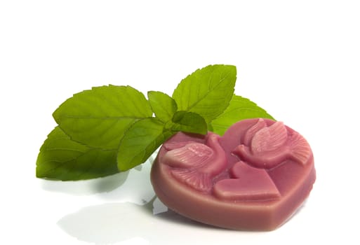 pink piece of soap in heart shape with green mint isolated on white